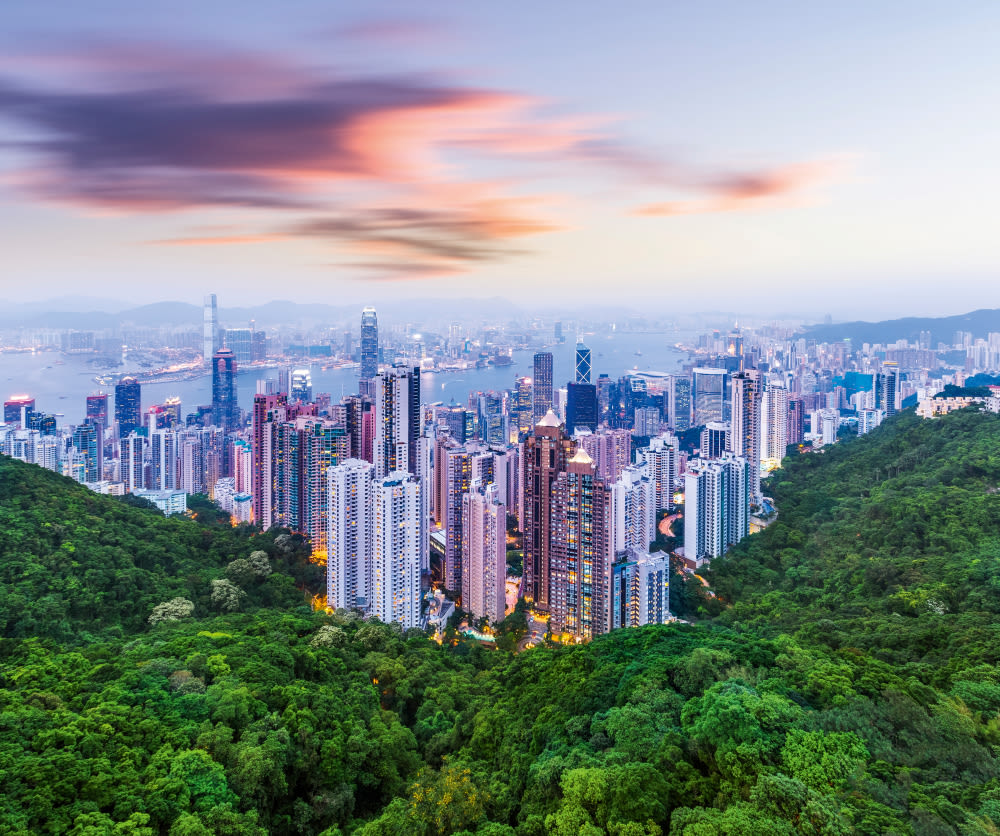 Hongkong Skyline bei Sonnenuntergang, Wolkenkratzer und grüne Hügel.