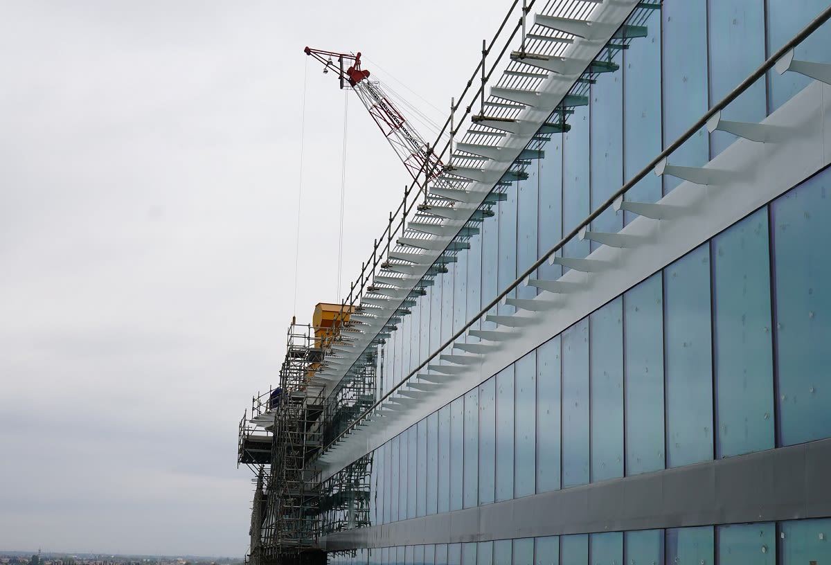 Kran und Gerüst an Glasgebäude, bewölkter Himmel.
