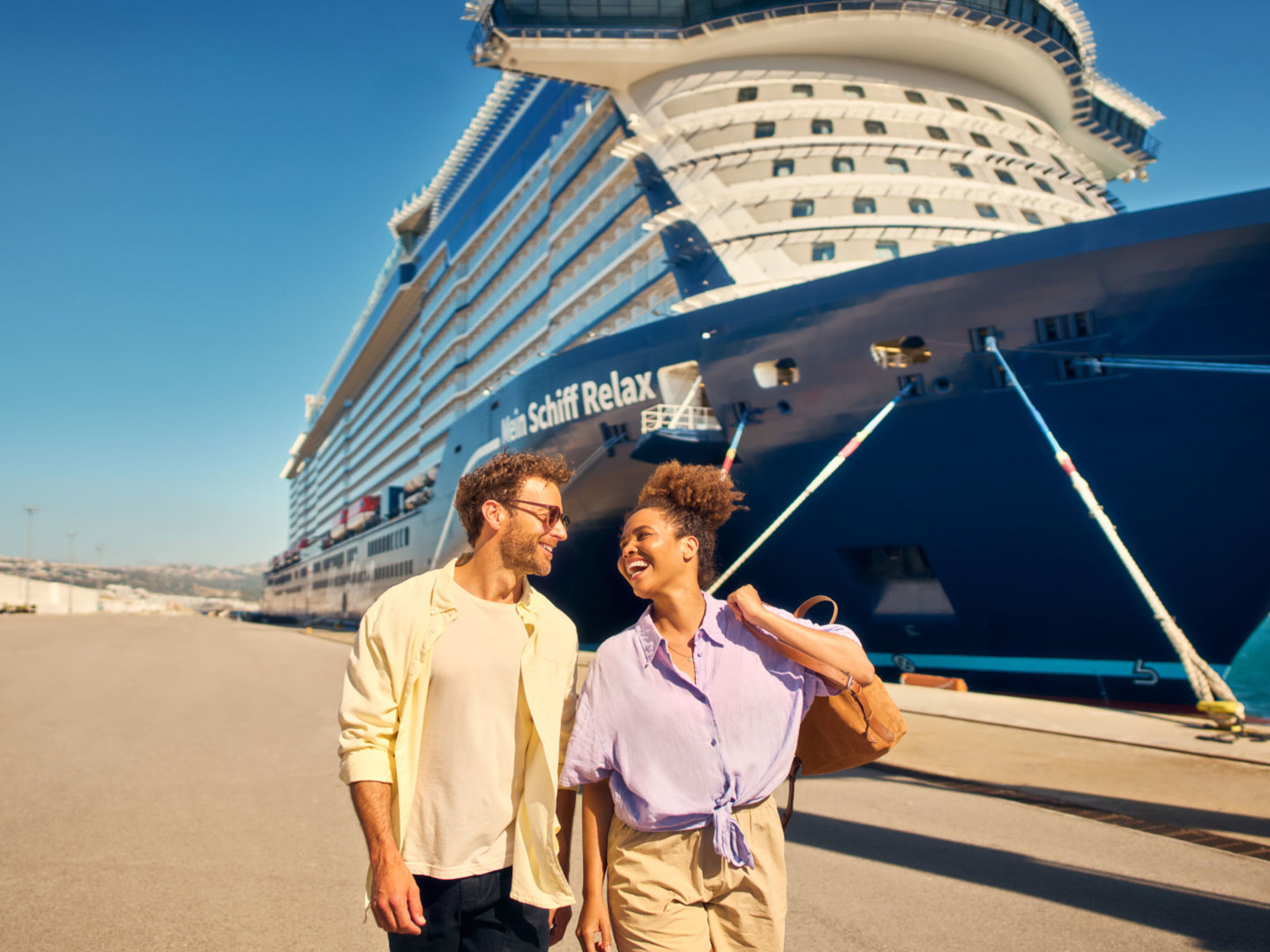 Paar spaziert vor Kreuzfahrtschiff der Mein Schiff® Flotte, sonniger Tag. Paar spaziert vor Kreuzfahrtschiff der Mein Schiff® Flotte, sonniger Tag.