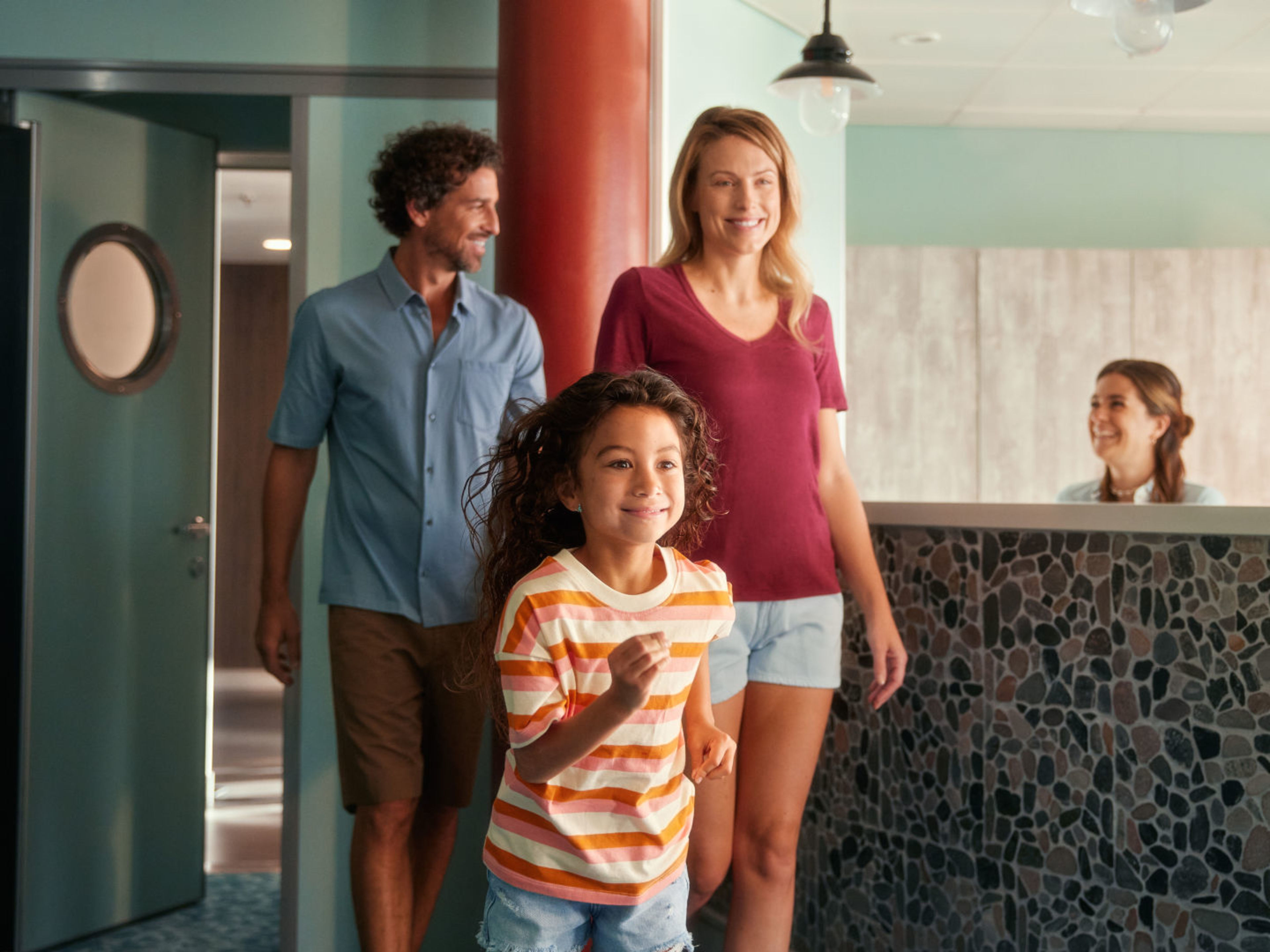 Eltern bringen Kind in den Kids-Club Familie betritt lächelnd Hotelrezeption, Empfangsdame begrüßt sie.