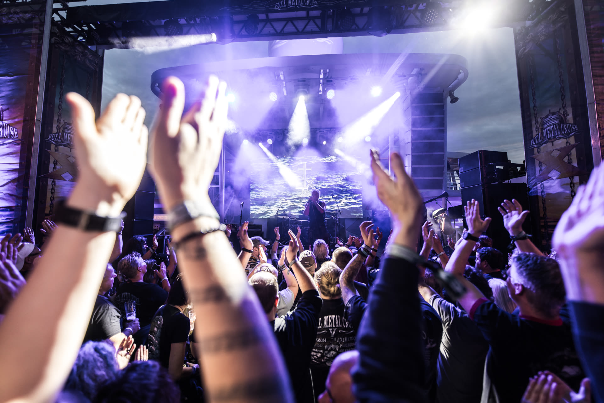 Konzert auf Kreuzfahrtschiff, jubelnde Menge, bunte Lichter, Abendstimmung.
