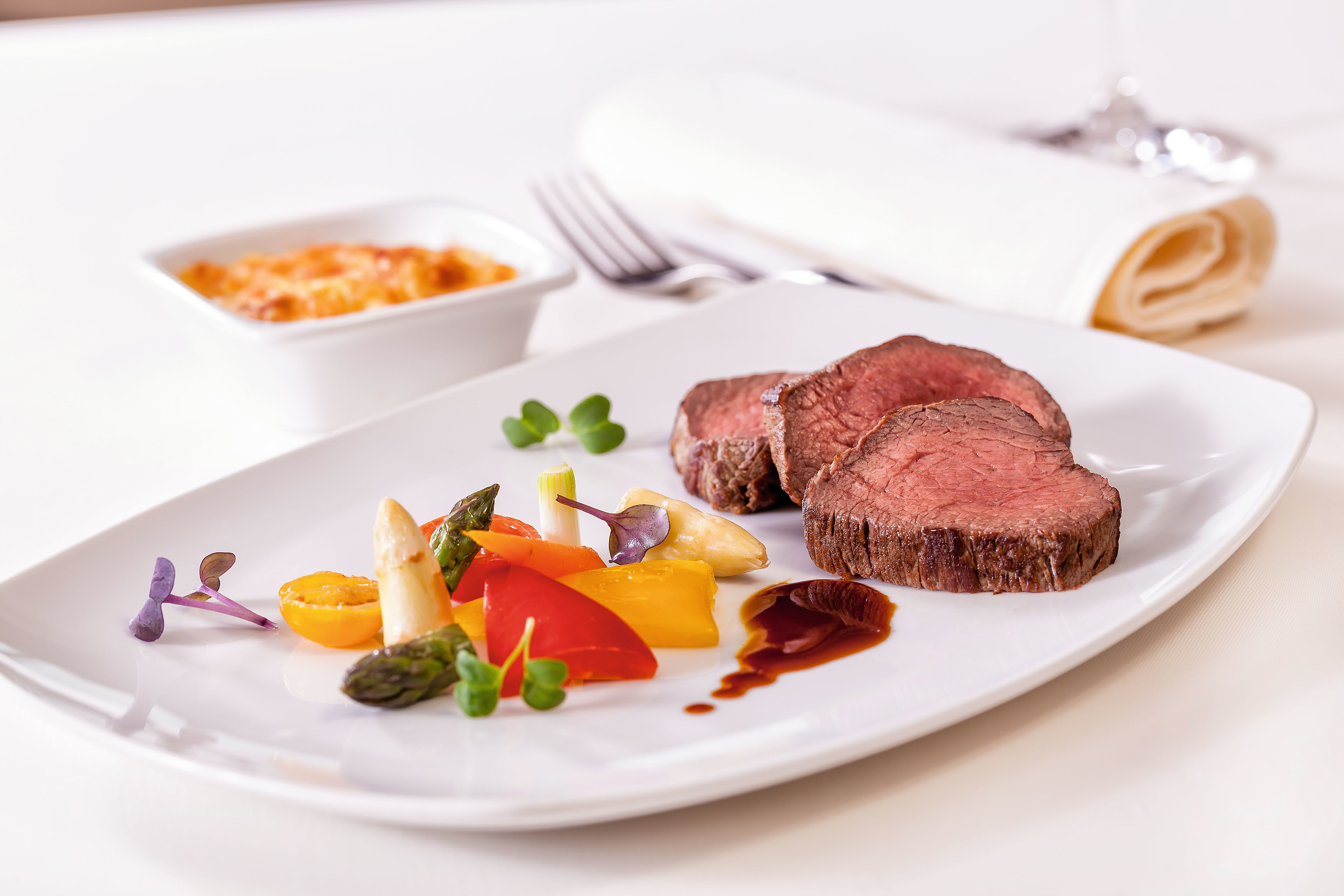 Rinderfilet mit Gemüse und Soße auf weißem Teller, elegant serviert.