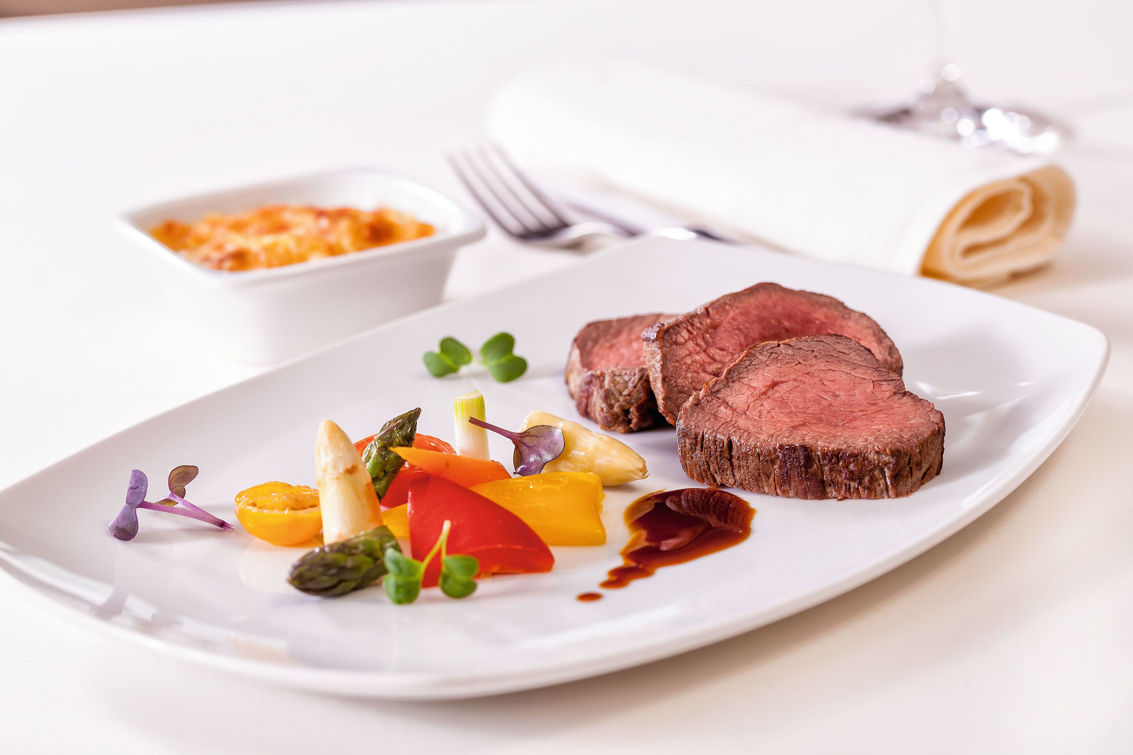 Rinderfilet mit Gemüse und Soße auf weißem Teller, elegant serviert.