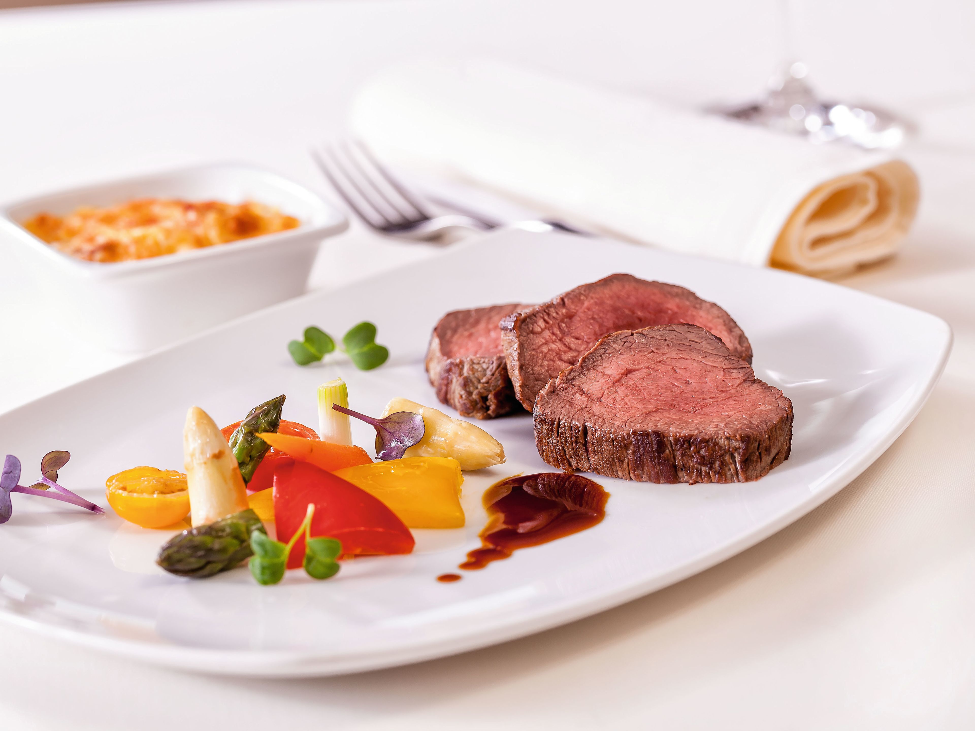Rinderfilet mit Gemüse und Soße auf weißem Teller, elegant serviert. Rinderfilet mit Gemüse und Soße auf weißem Teller, elegant serviert.