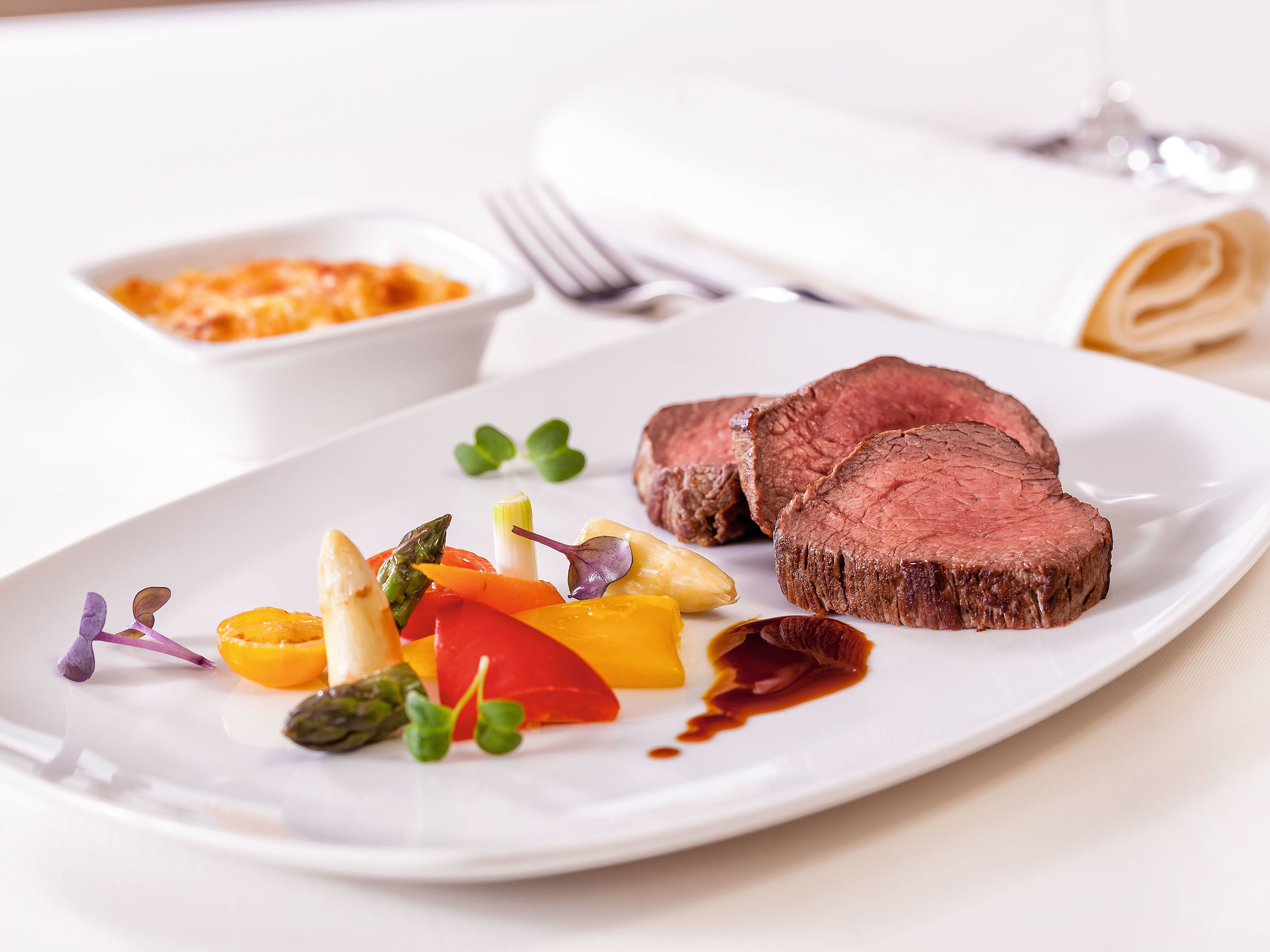 Rinderfilet mit Gemüse und Soße auf weißem Teller, elegant serviert. Rinderfilet mit Gemüse und Soße auf weißem Teller, elegant serviert.