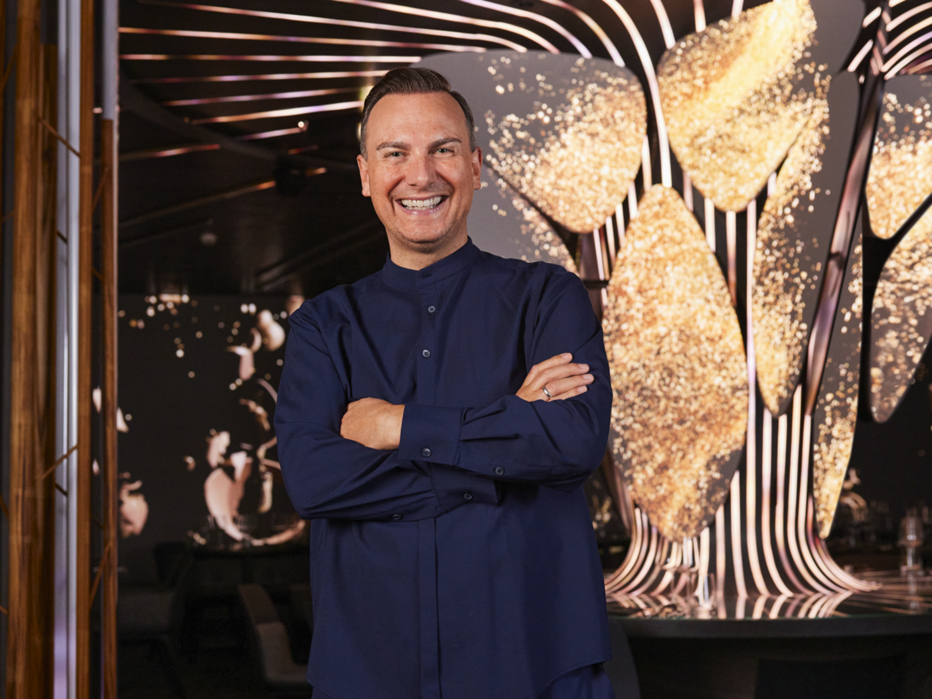 Tim Raue vor einem goldenen Hintergrund Tim Raue vor einem goldenen Hintergrund