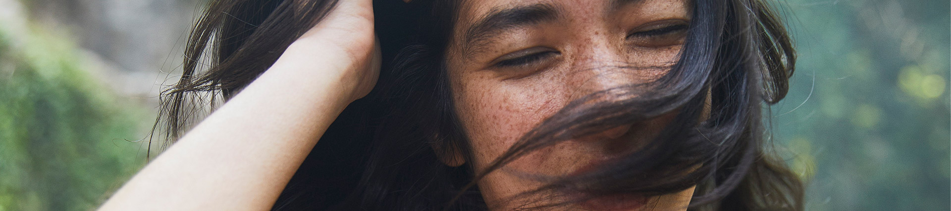 Dark haired woman in burnt orange top smiles under bamboo leaves