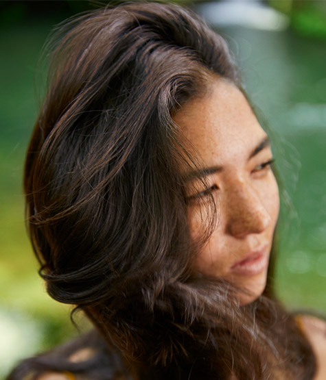 A model with long dark hair smelling an ingredient