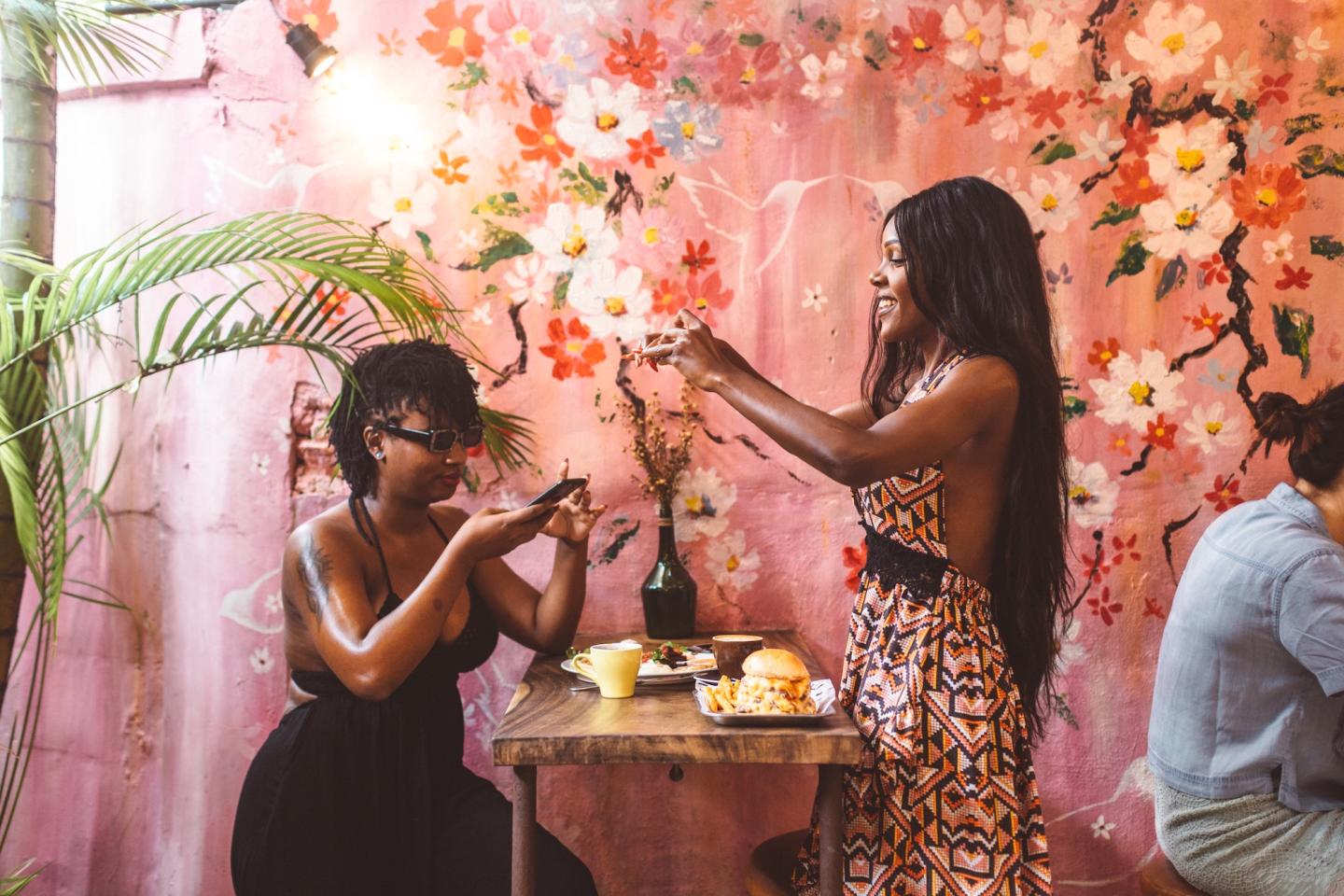 2 women taking photos of their food in a pink and flowery restaurant