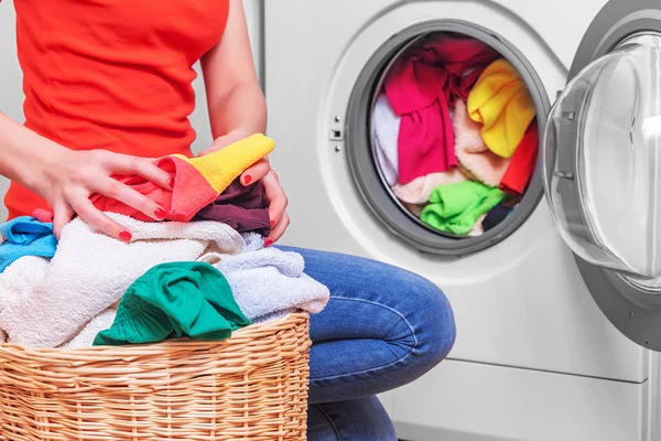 Woman with basket of laundry in front of washing machine.