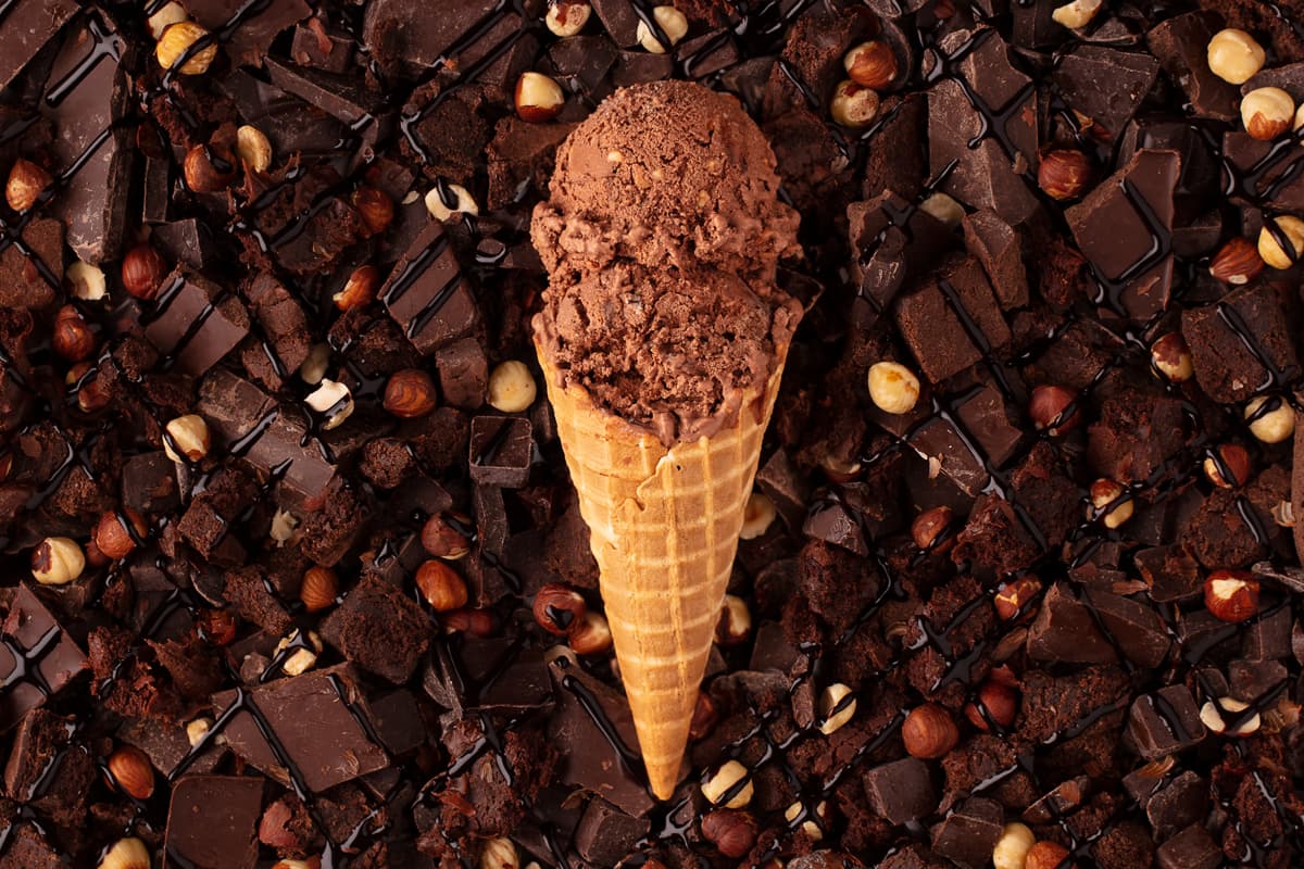 Waffle cone with 2 scoops of grass-fed dairy chocolate ice cream lying on a bed of decadent dark chocolate