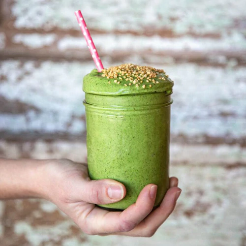 Delicious green smoothie in a mason jar with a pink and white poke-a-dot straw being held in a hand. 