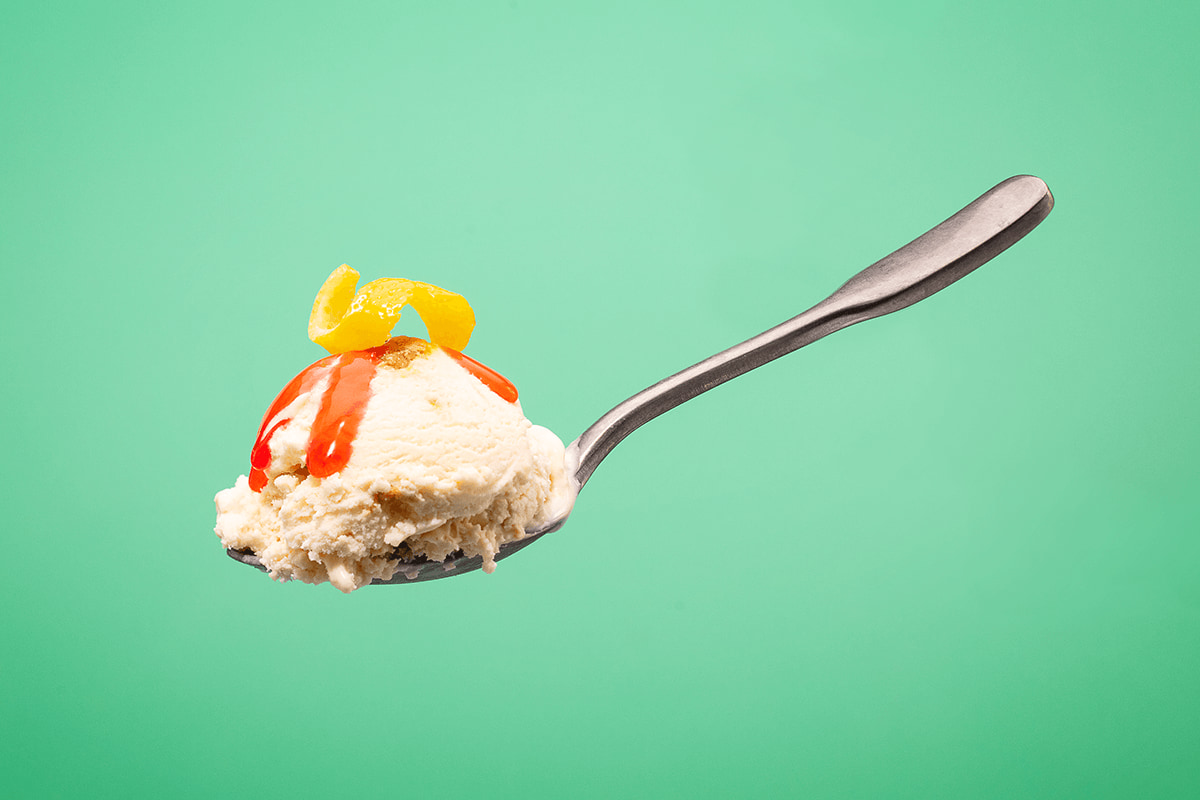 Strawberry Lemon Plant-Based Ice Cream on a spoon topped with strawberry sauce and a lemon peel. 