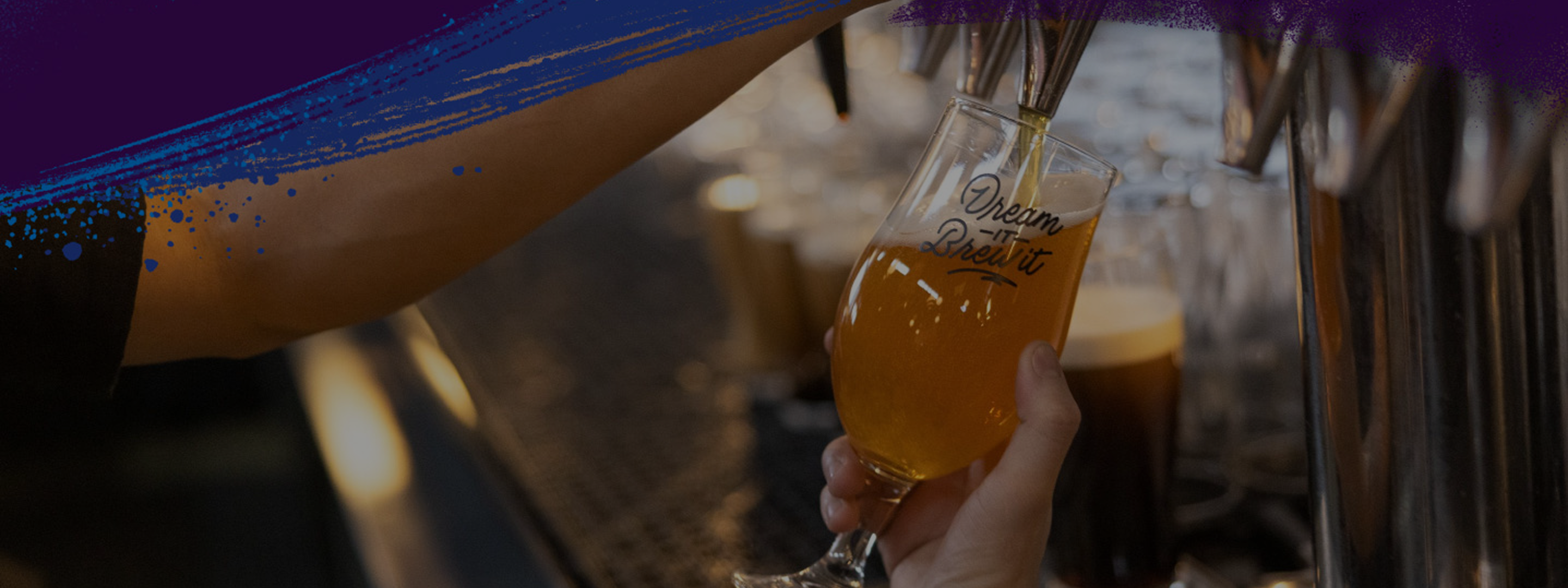A person fills a glass of beer from a tap; the glass reads "Dream it Brew it" and there are colorful paint splatters at the top of the image.