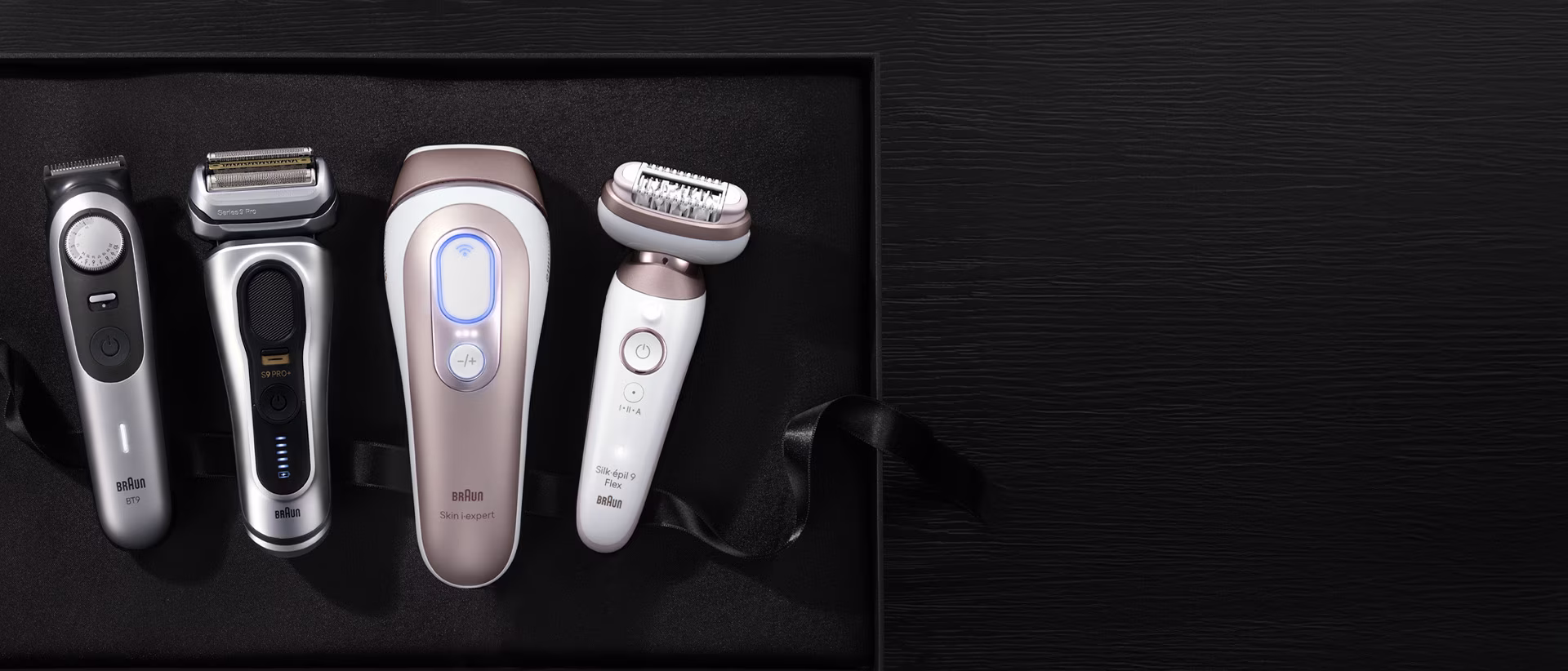 Quatre produits Braun dans une boîte noire. De gauche à droite : une tondeuse à barbe argentée, un rasoir électrique argenté, un appareil d'épilation à lumière pulsée (IPL) or rose et blanc, et un épilateur électrique or rose et blanc.