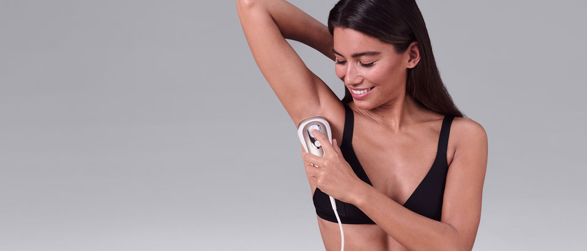 Une femme souriante en train d'utiliser un appareil d’épilation à lumière pulsée Braun à domicile sur ses aisselles