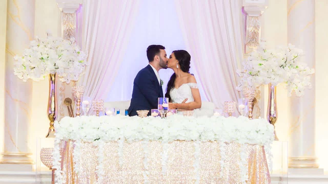 The kissing couple at the wedding's head table. Taken by Samantha Ong from Ivanna + Gaurav's wedding. Attribution: https://samanthaongphoto.com/paradise-banquet-hall-wedding/