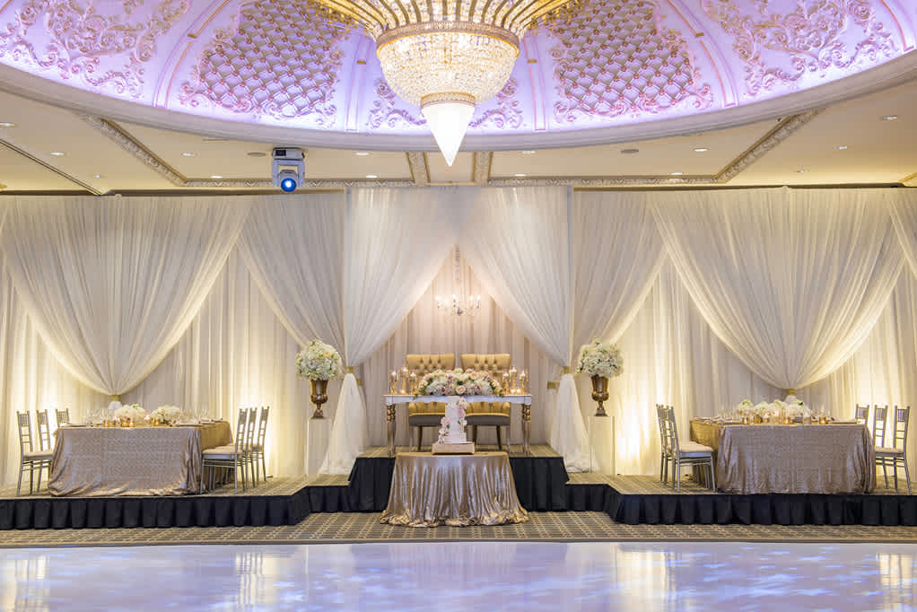 An interior shot of the Classic room focusing on the main Bride and Groom seat with the cake in front with the chandelier overhead and the dance floor in front.