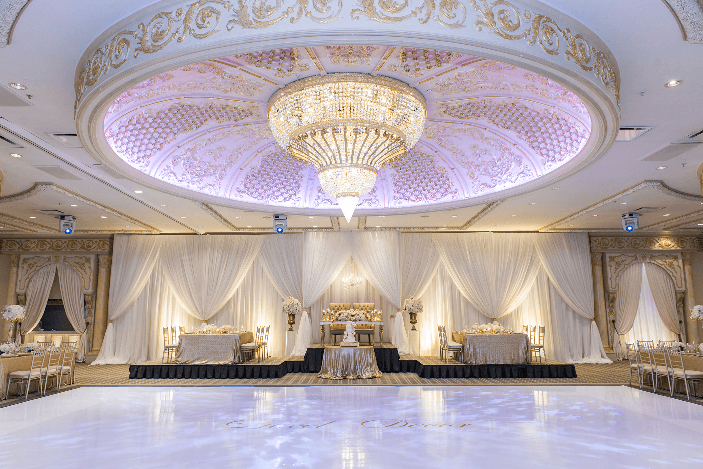 A wide shot of the hall showing the large chandelier on the ceiling, expansive dance floor, and seating arrangements.