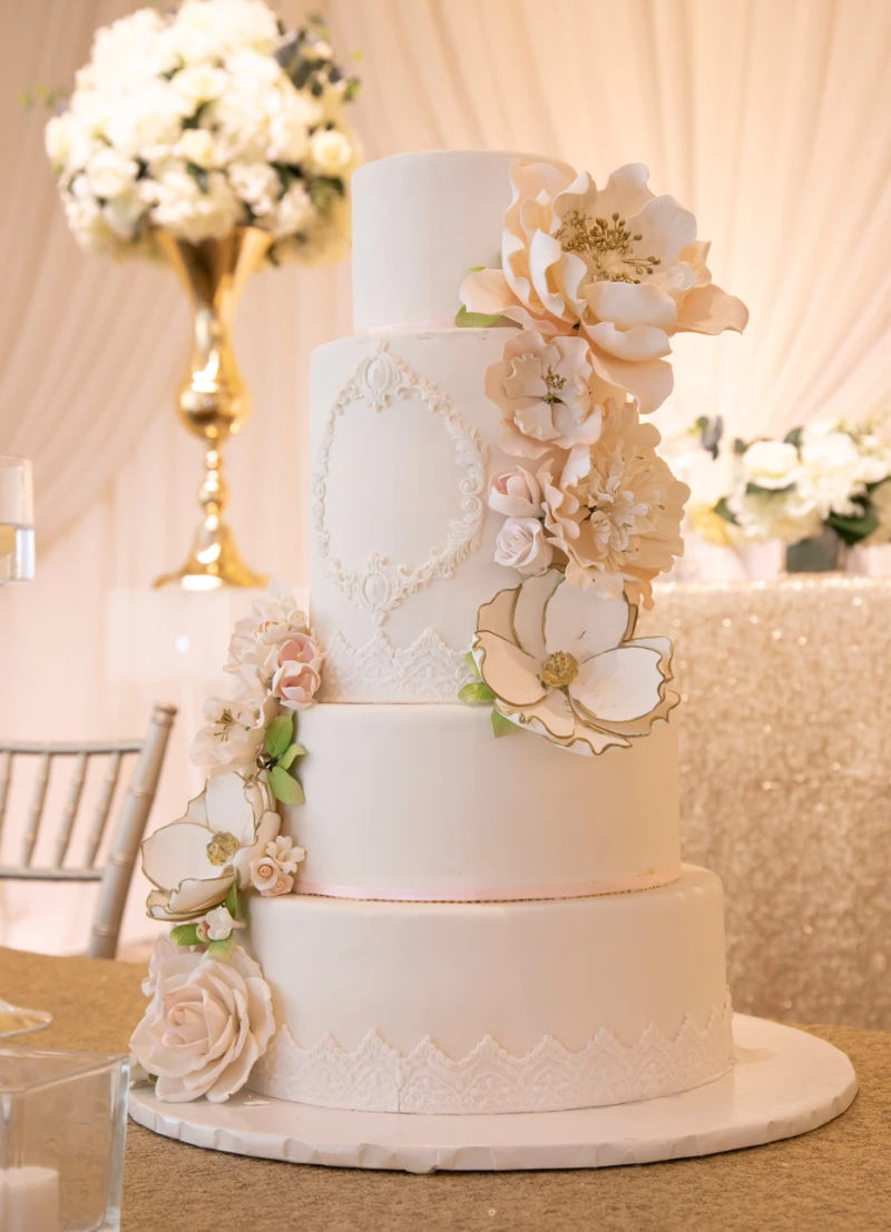 A white, 4-tier wedding cake decorated with flowers.