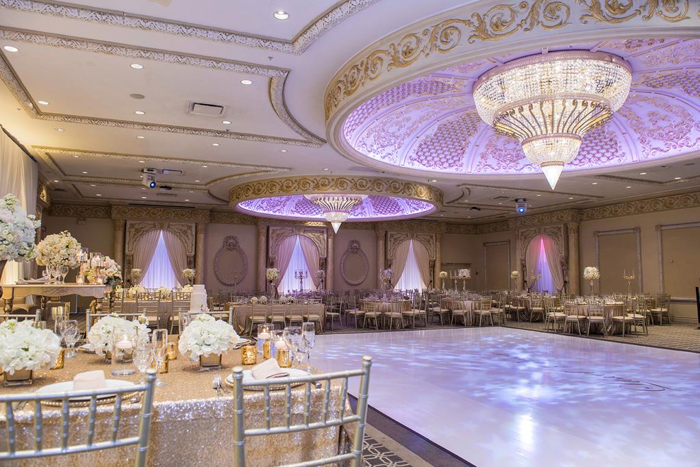 Wedding seating surrounding the dance floor over which a giant chandelier with light purple lighting.