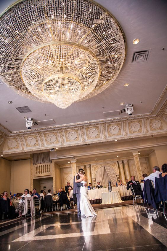The lucky couple dancing on the ballroom floor below the room's gigantic chandelier.