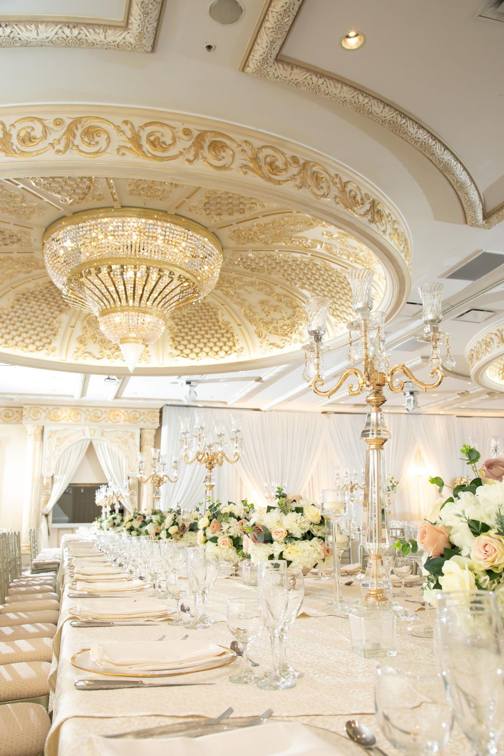 One of Paradise Banquet Halls' many chandeliers overtop a white and light pink themed table set.