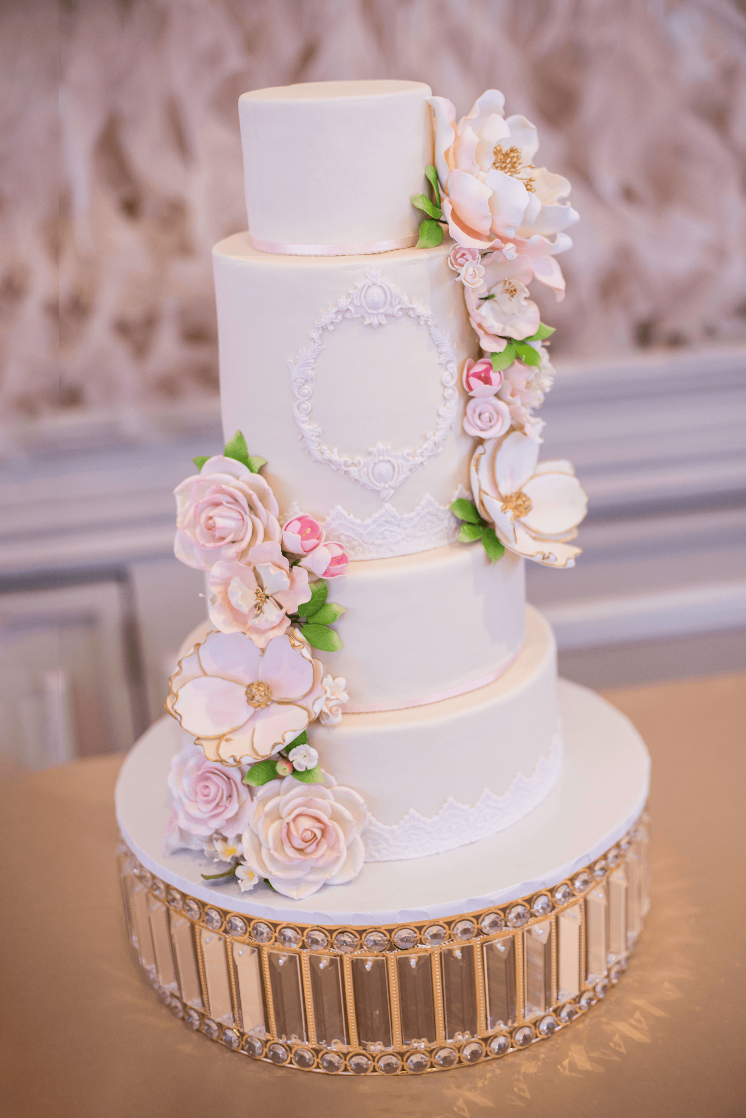 A white, 4-tier wedding cake decorated with flowers.