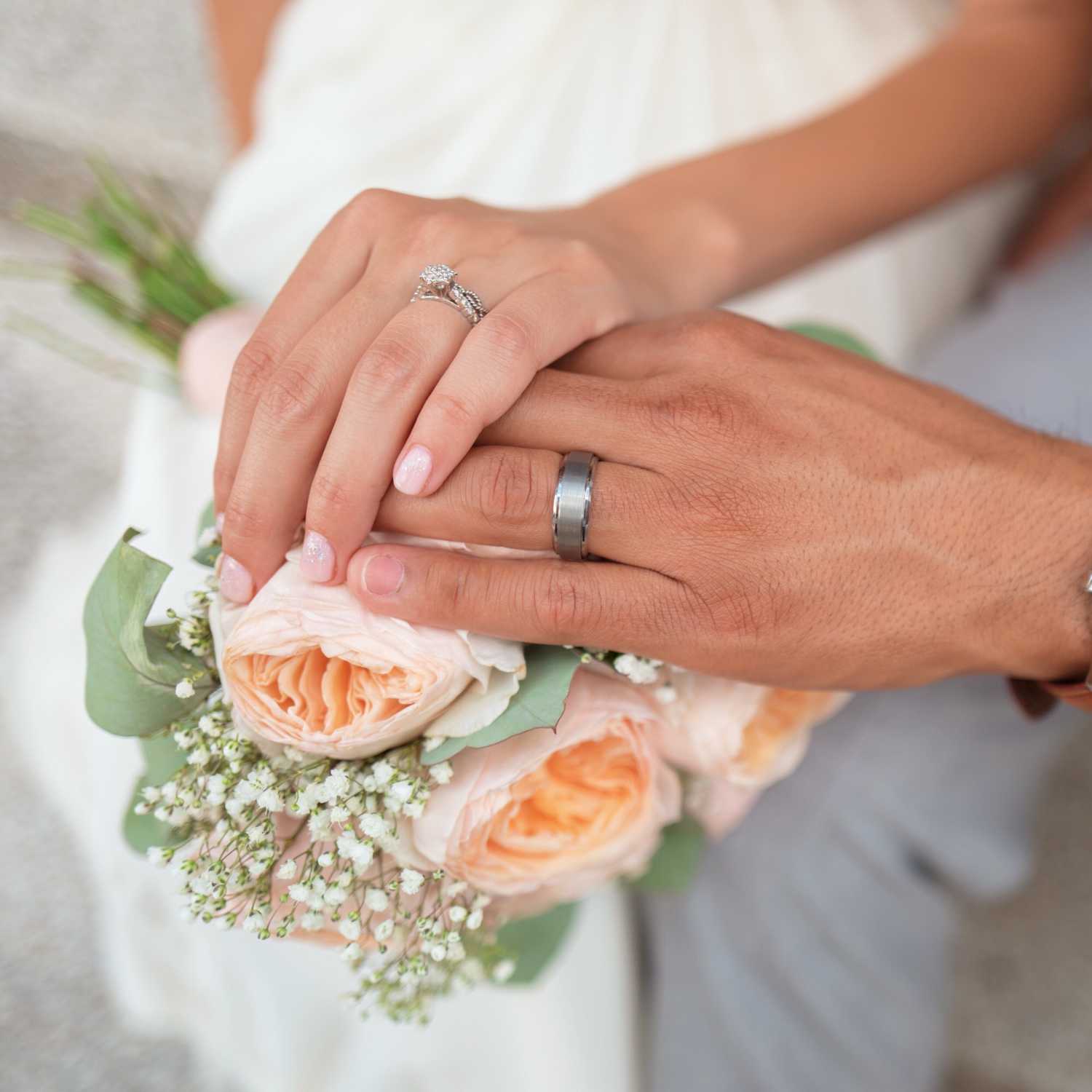 A wedding couple showing their rings over a bouquet of flowers.