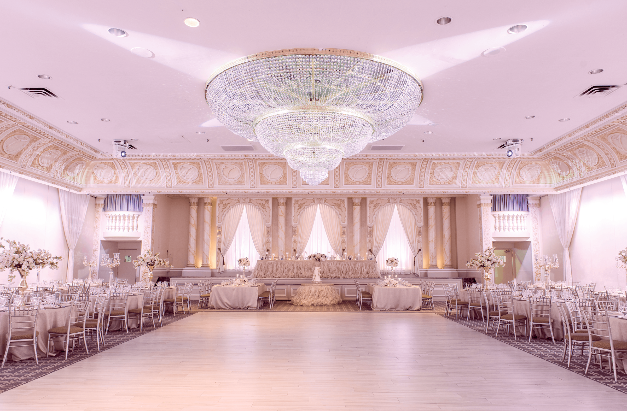 A wide shot of a ballroom with a dance floor and a chandelier.