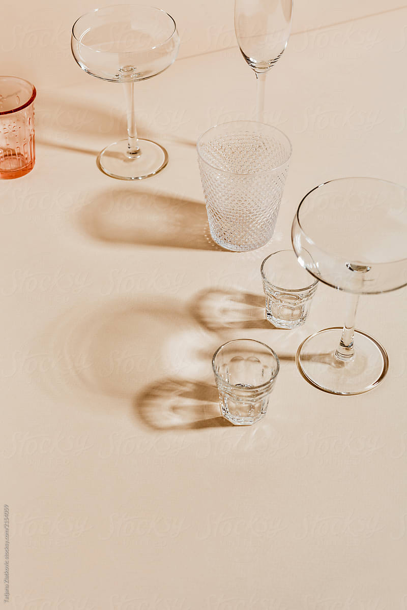 A loose collection of clear crystal glasses of various type with light passing through them onto a light, peach-coloured tabletop.