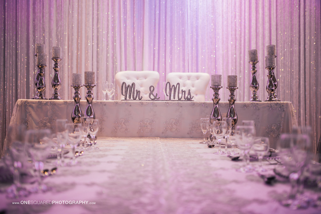 The head table at a wedding decorated in pink with a Mr. & Mrs. sign and candles.