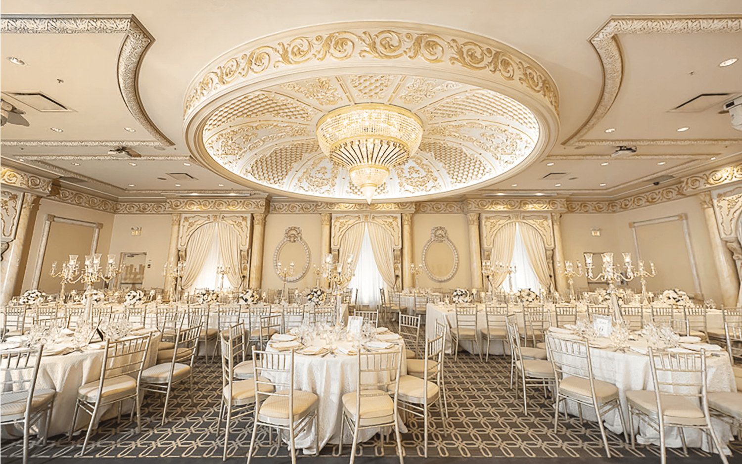 A wide shot of the Classic Ballroom at Paradise Banquet Halls with a large chandelier, ample seating for 450 people, and large dance floor.