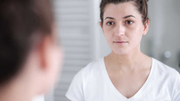 Frau mit Neurodermitis betrachtet sich im Spiegel