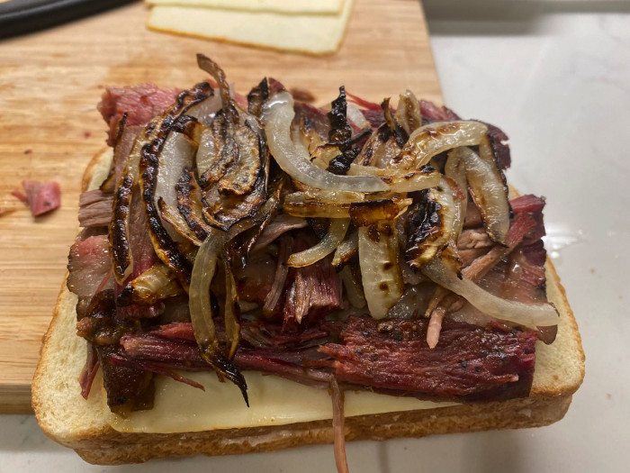 A half-open sandwich with cheese, brisket, and grilled onions.
