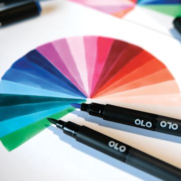 Open in modal - Olo Dual-Tip Markers, two brush markers laid out over drawing of a color wheel
