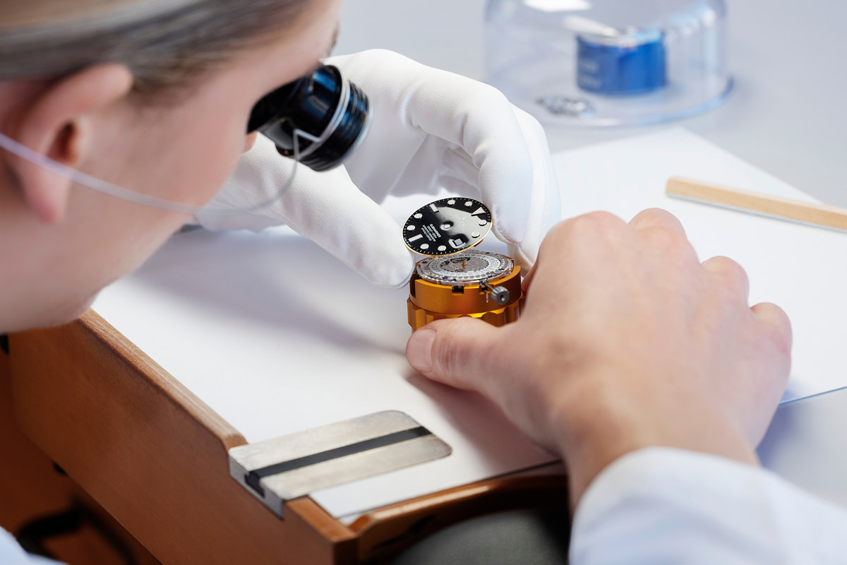 Rolex watchmaker fitting a dial with a loupe