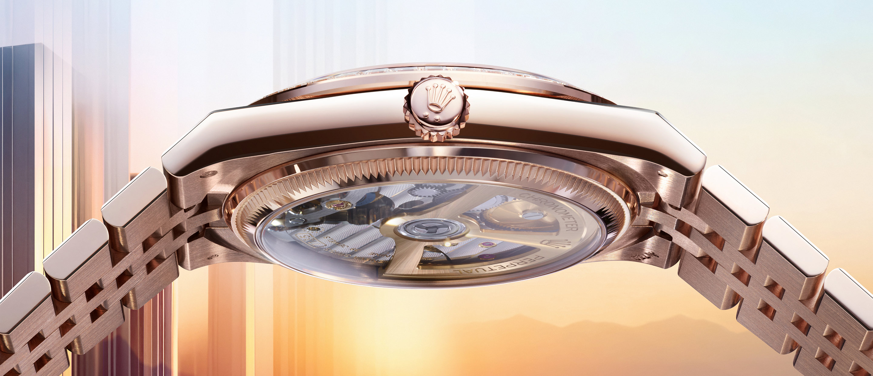A close-up shot of a luxury wristwatch with a metallic silver band and a mother-of-pearl dial. The watch displays the day and date, with the day shown in an arc window at the 12 o'clock position and the date at the 3 o'clock position.