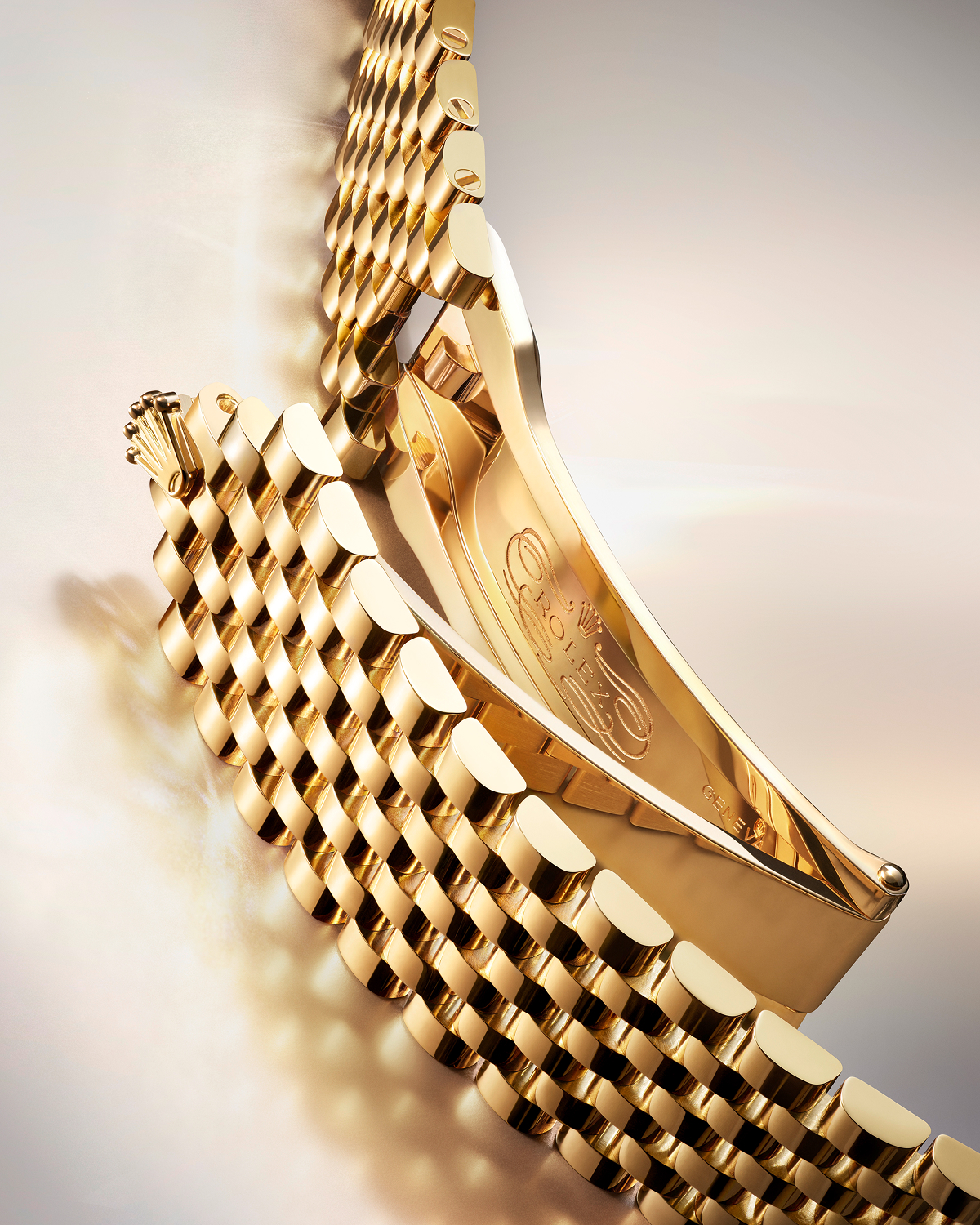 Close-up image of a high-end wristwatch's leather strap and clasp. The strap is brown with a crocodile pattern, and the clasp is metallic with a polished finish, featuring an embossed logo of a five-pointed crown. The background is a smooth, light surface.