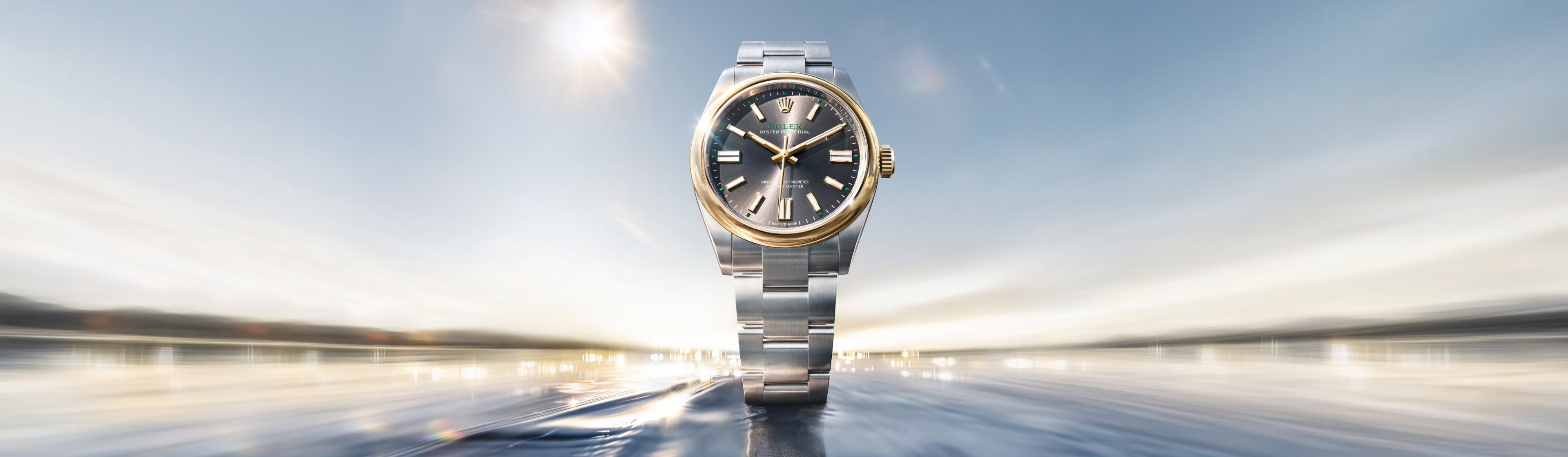 A luxurious wristwatch with a silver case, a black strap, and a detailed white dial featuring multiple sub-dials and gemstone embellishments is displayed against a gradient background transitioning from blue to light gold, suggesting a sunrise or sunset.