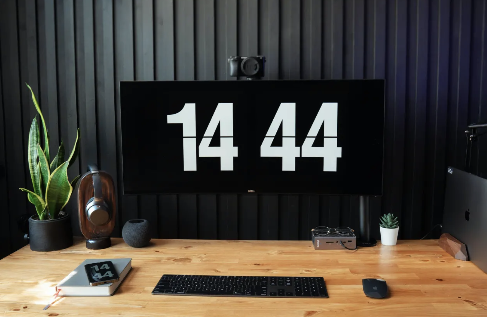 A nicely designed desk with a big monitor showing a clock.