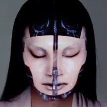 Screenshot of video of an artificial woman with an "open" forehead showing mechanical brain and a face that is splitting open down the middle with a small view of the components behind it.
