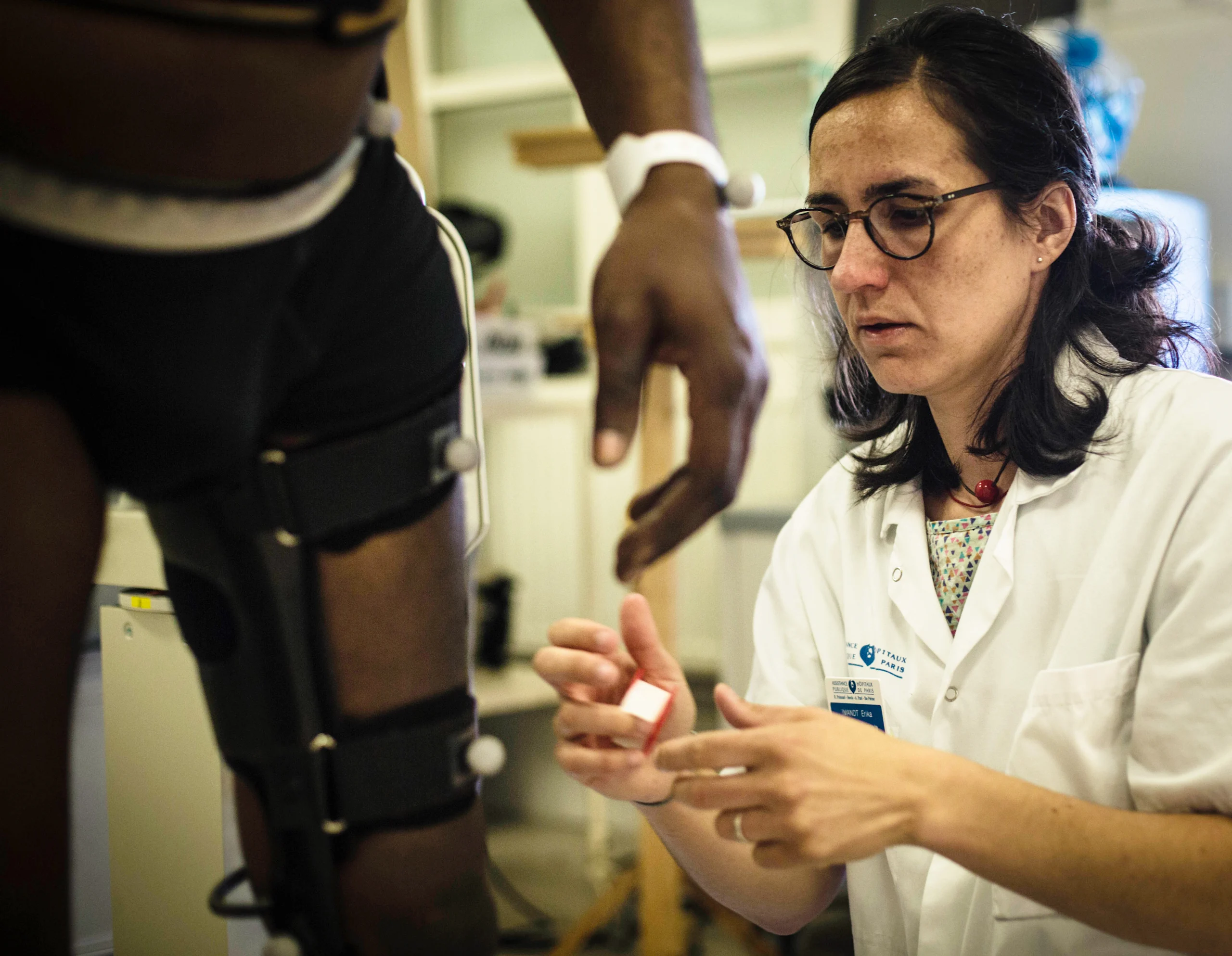 A nurse works on the leg brace covering a man's leg. The brace has motion tracking / capture devices on it.