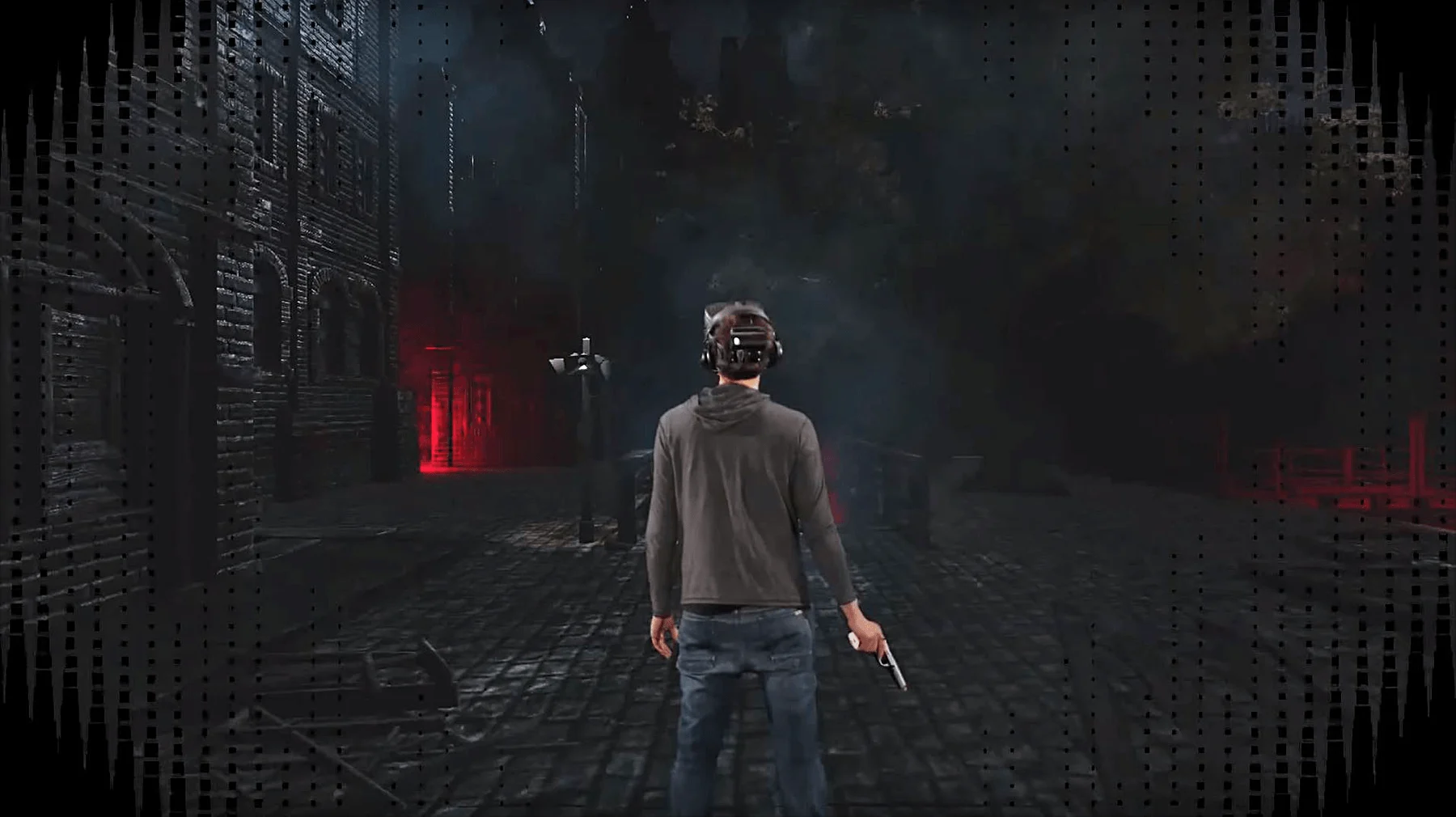 A picture behind a person wearing blue denim jeans, a gray hooded shirt, and a VR headset standing in a virtual reality environment with black buildings and road and a red light in the distance.