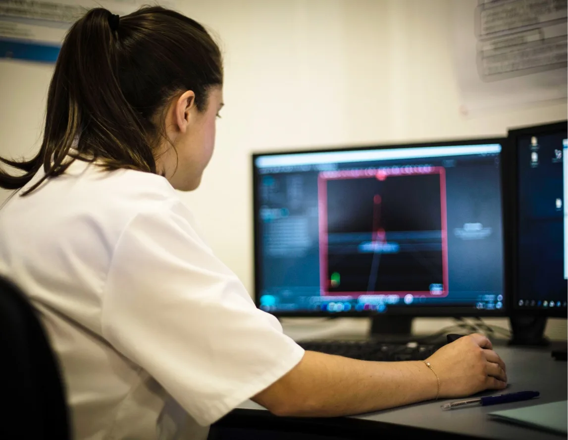 Woman in white shirt sitting at a desk with two computer monitors looking at OptiTrack system