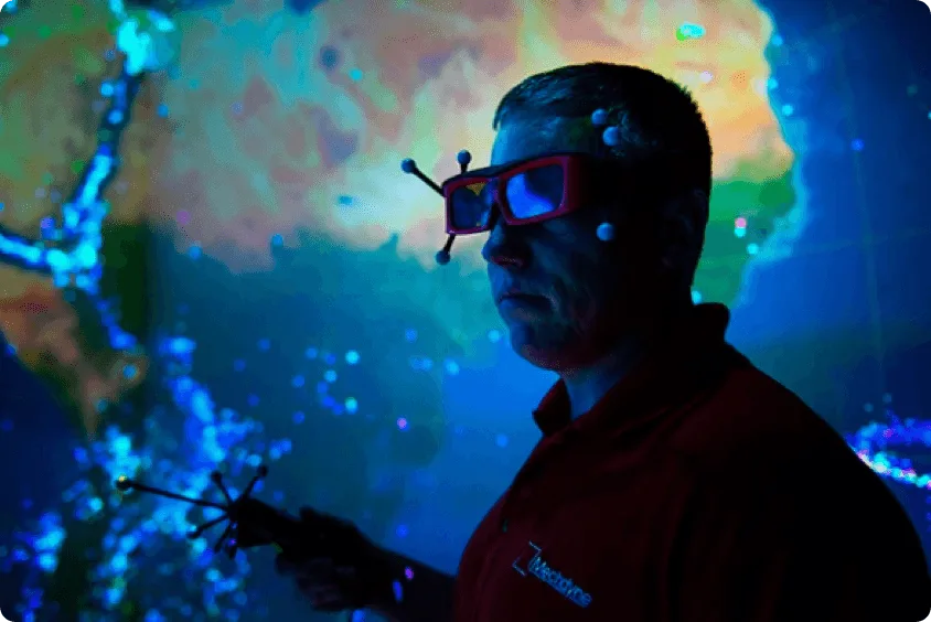 Person in a dark environment wearing 3D (or something similar) glasses that have virtual reality trackers (small white balls attached to the end of short pegs coming out of the glasses). The background is a space-like environment with multiple colors possibly suggesting a nebula.
