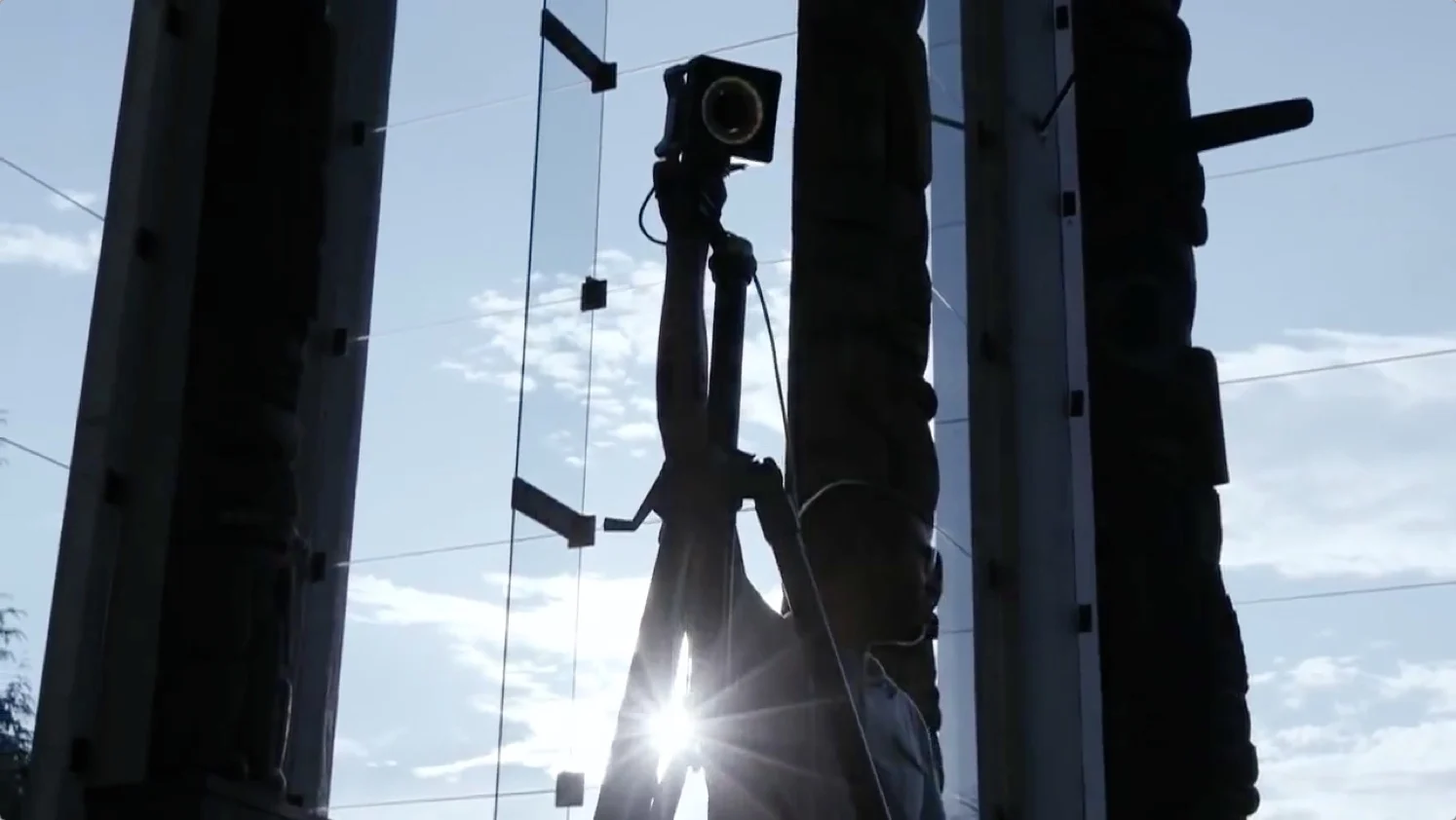 Silhouette of a person holding an OptiTrack camera on top of a tripod with the sun in the background