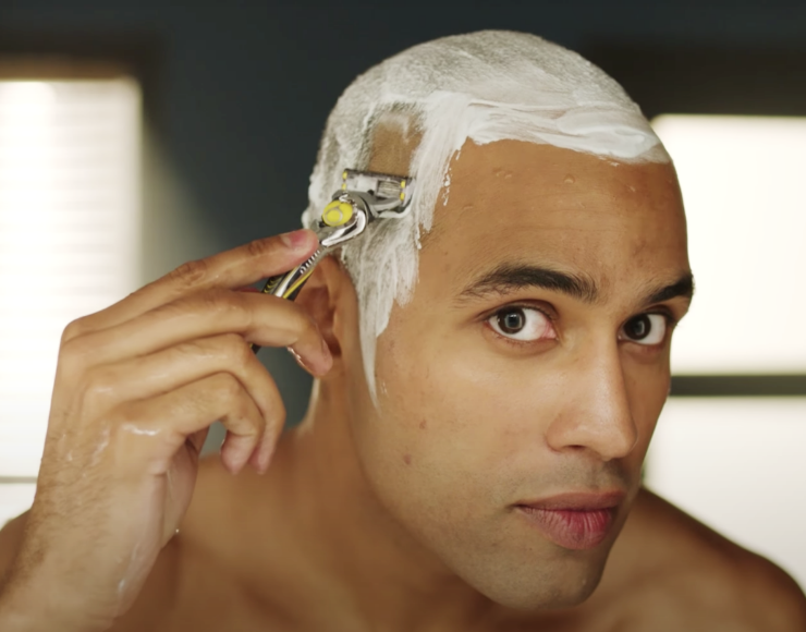 Hombre caucásico tratando de afeitarse la cabeza con una
