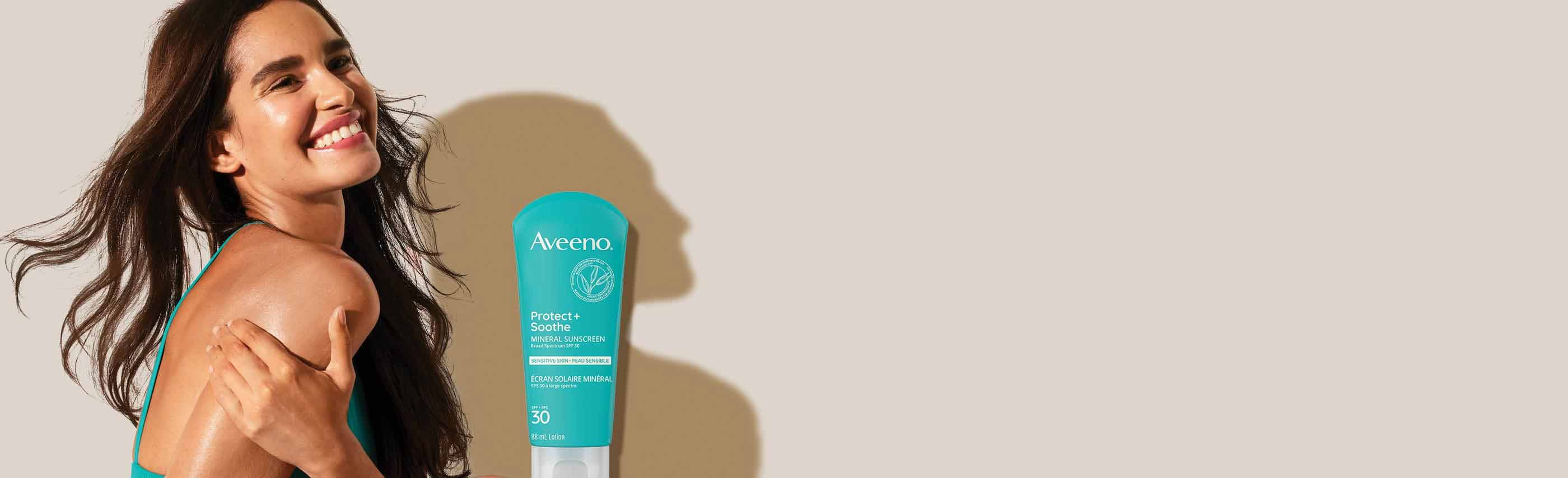 woman with long brown hair smiling and AVEENO® Protect & Soothe SPF 30 mineral sunscreen for face, squeeze tube, 88 mL