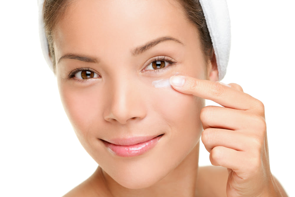 Young woman applying eye cream under her left eye